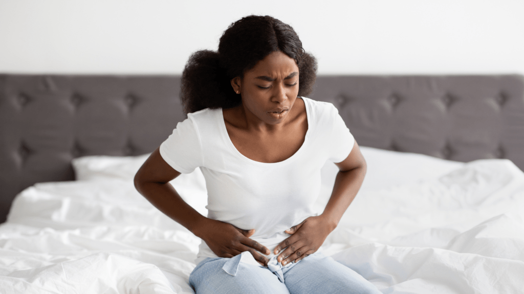 Women holding her stomach in pain at the end of her bed
